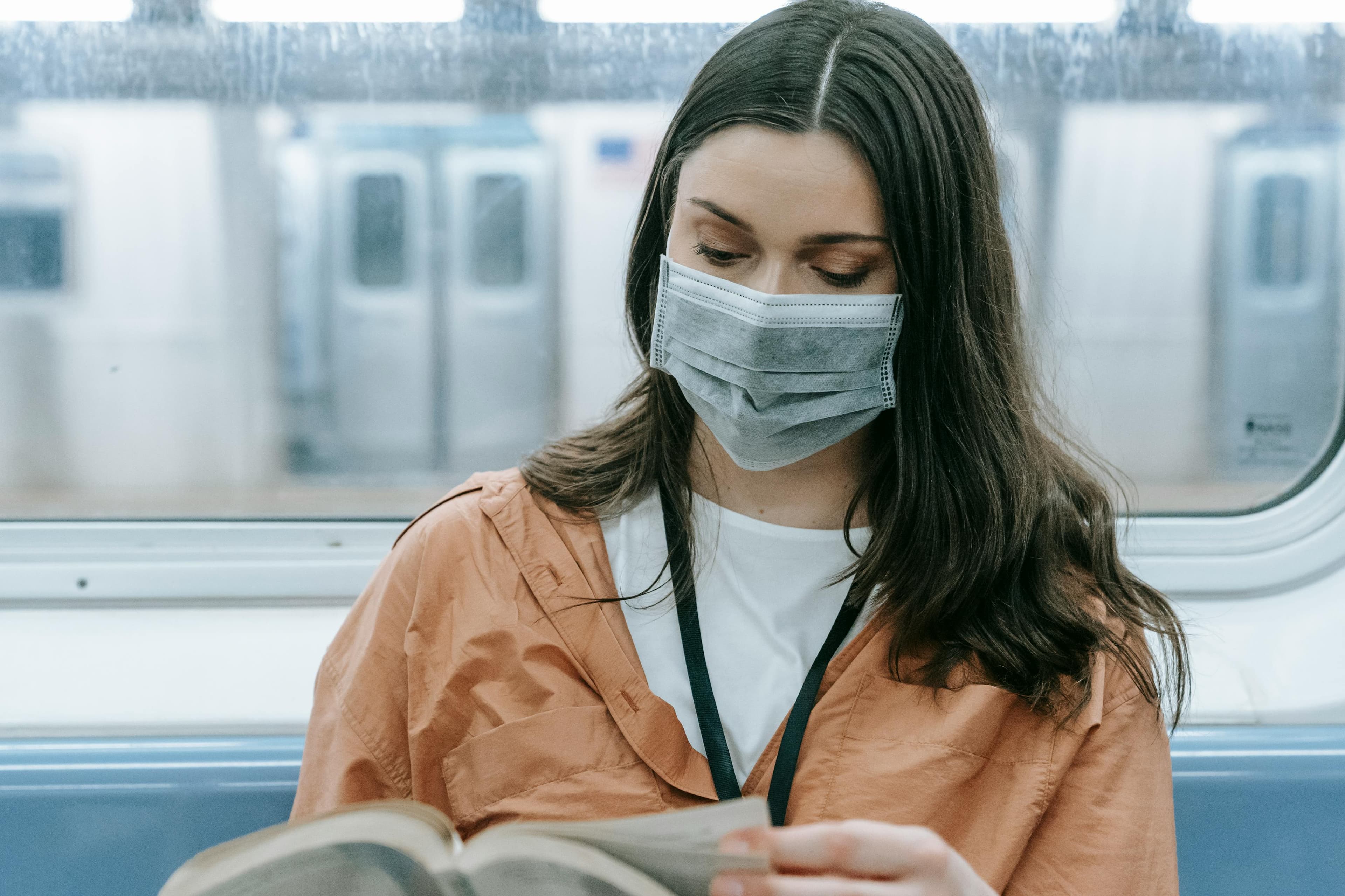 Picture of a young woman riding the subway wearing a mask and reading a book